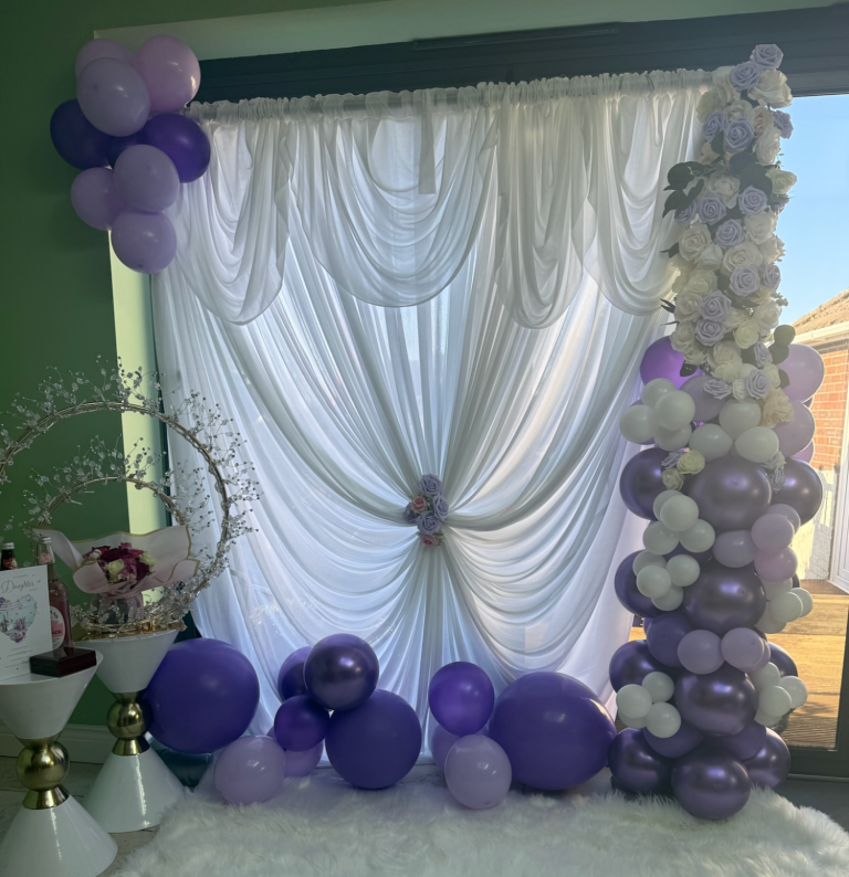 Purple themed backdrop A decorative setting with white drapes, purple balloons, and floral accents.